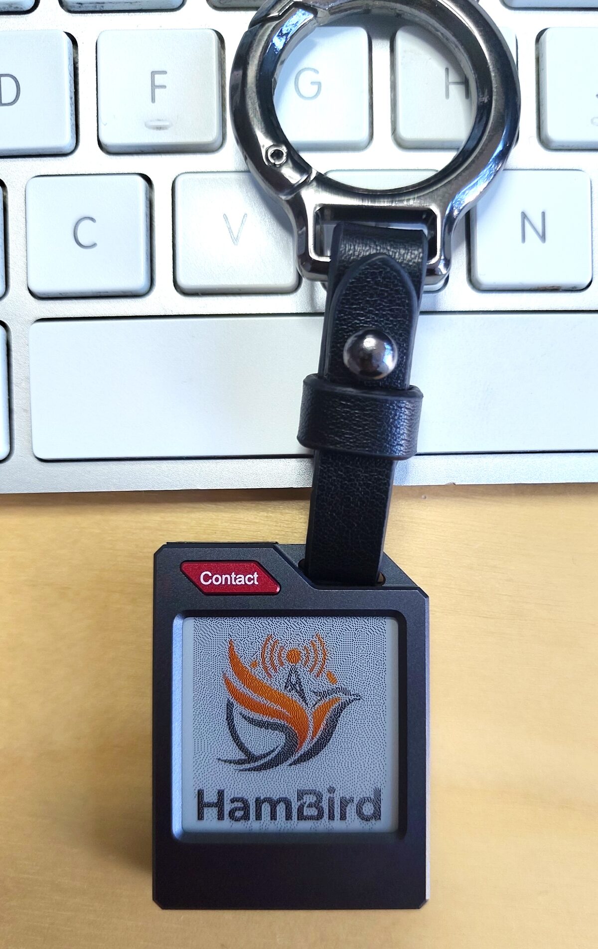 HamBird-Empfänger am Schlüsselbund vor einer Tastatur: schwarzes Gehäuse, rote Contact-Taste, 1,54-Zoll-E-Ink-Display mit HamBird-Logo